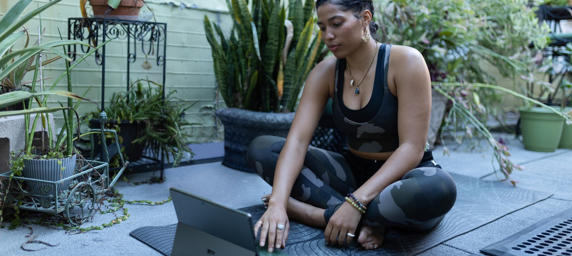 Woman working at a laptop outdoors, on a deck surrounded by plants