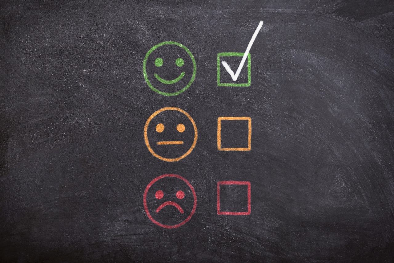 A blackboard with a three smiling faces and three tickboxes in a colomn. The first face in smiling and in green. The second is neutral in orange. The final is red and frowning. The first box is ticked. Image credit: Adrian from Pixabay