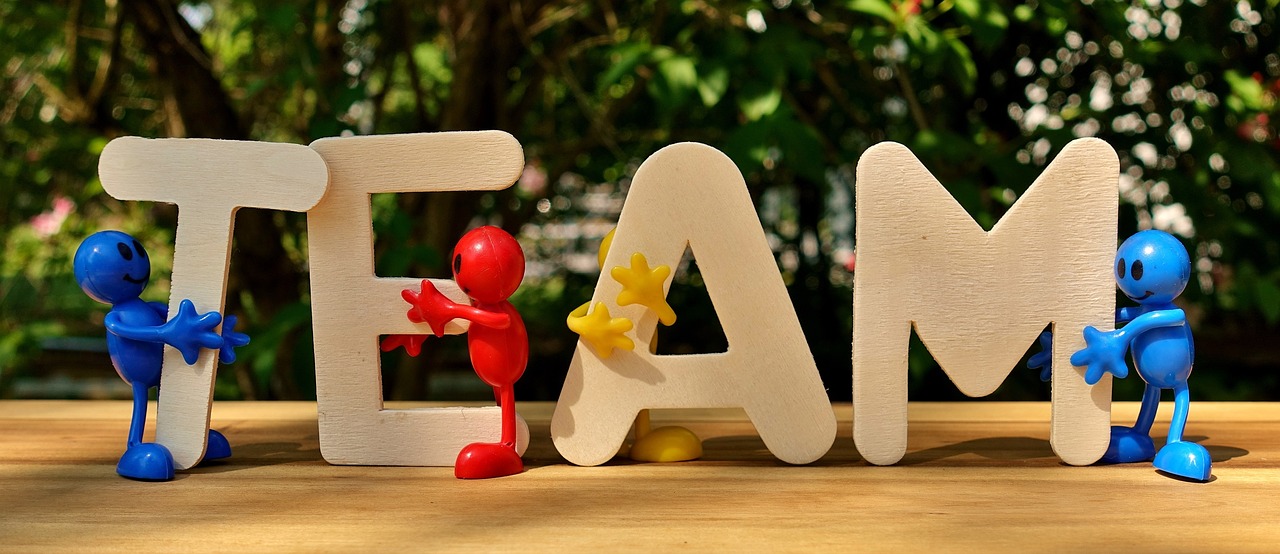 Cut wooden letters spelling the word 'team' with multi-coloured figures helping to support them.
