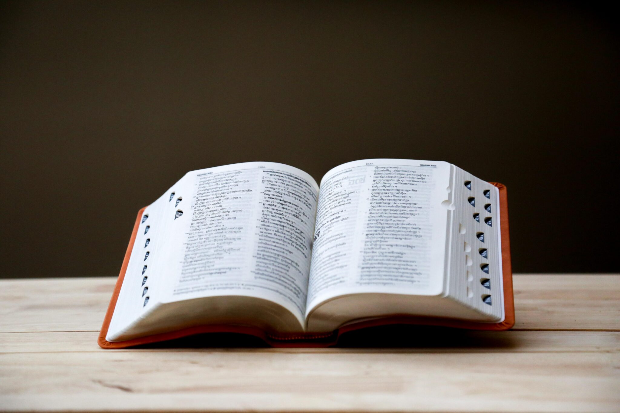 An open dictionary on a table, with a glimpse of a red cover peeking out from the pages.