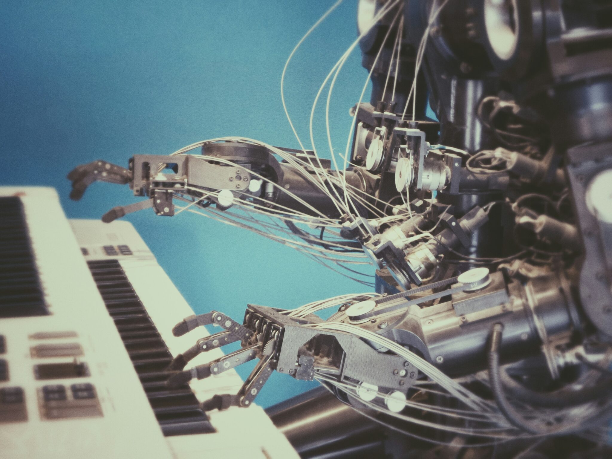 A metal robot made up of lots of joined, angular parts, sitting at a piano to play it.