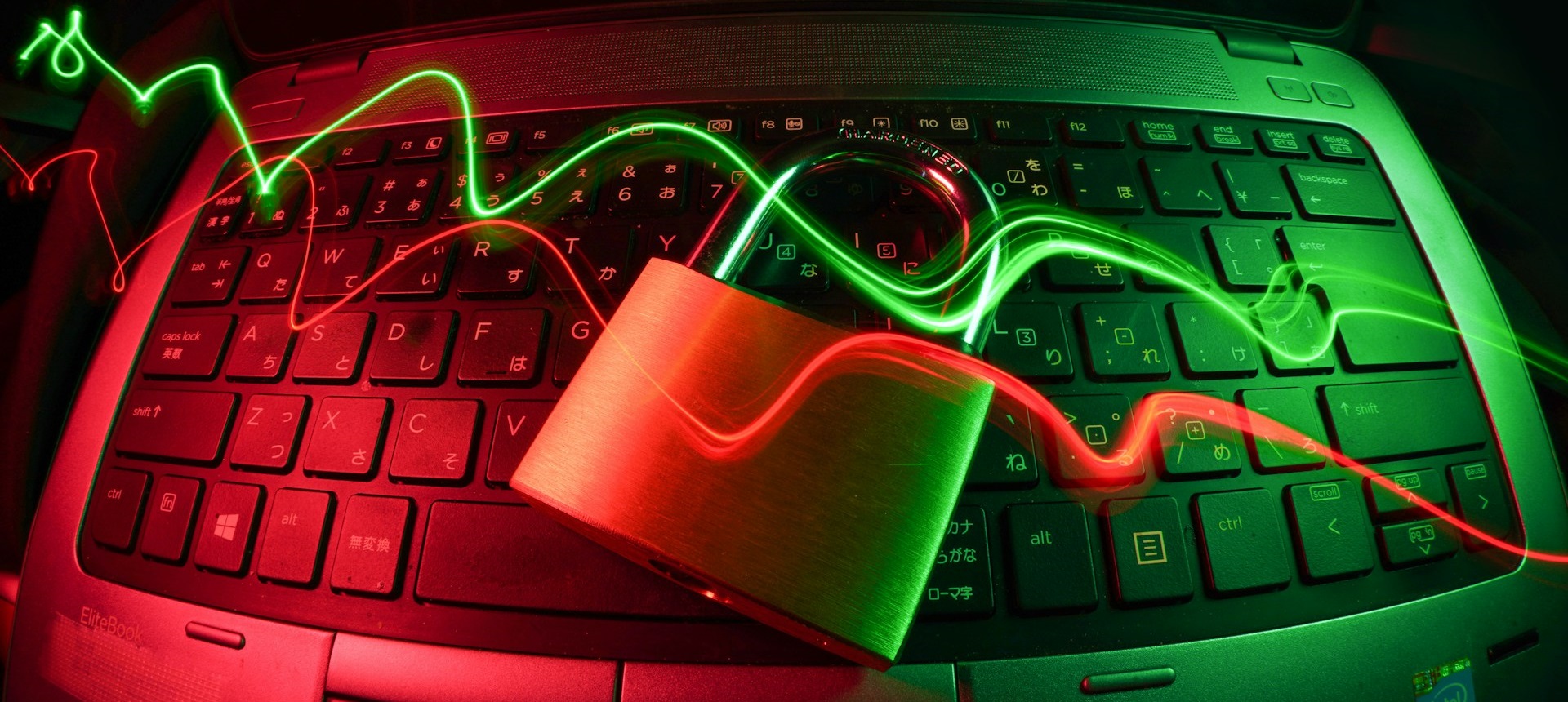 Computer keyboard overlaid with wavy beams of green and red light and a padlock. Photo by FlyD on Unsplash