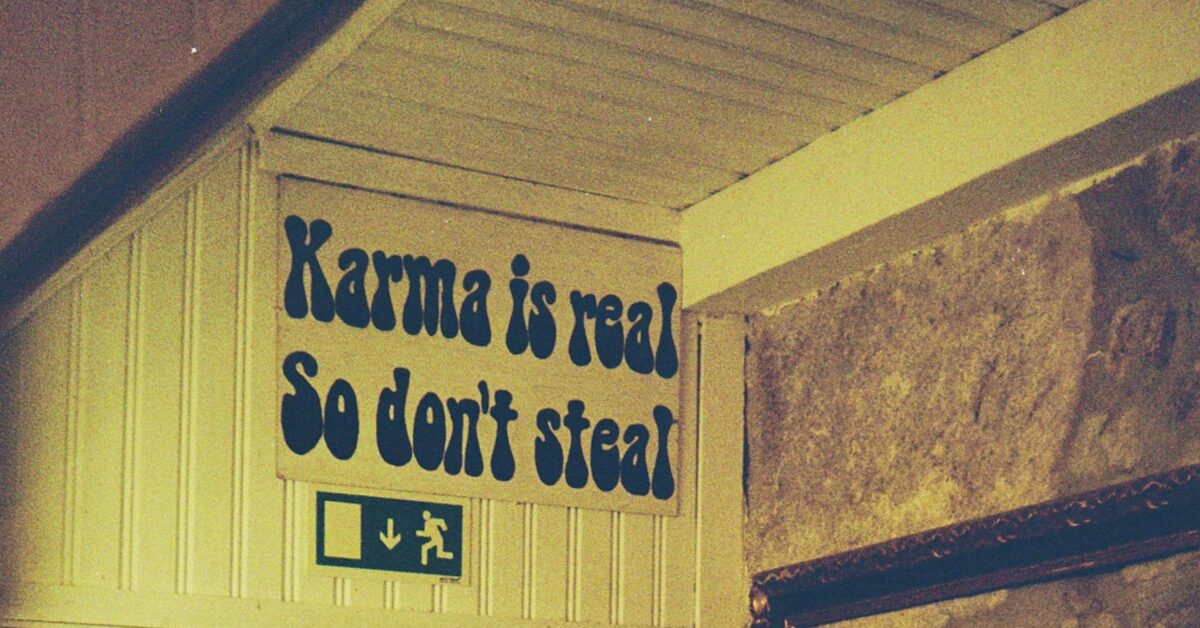A corrugated metal wall, with a yellow tint, which has a sign that says "Karma is real so don't steal" on it.
